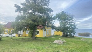 A yellow house with a red roof, surrounded by a grassy area and large rocks.