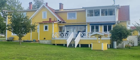 A two-story yellow house with a balcony, a small porch, and a flag on top.