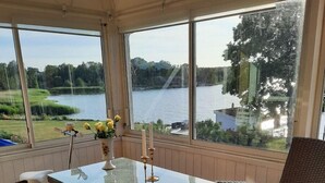 A sunroom with a glass table, wicker chairs, and a view of a lake.