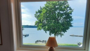 A bench with a striped cushion, a lamp, and a view of a lake with a tree and dock.