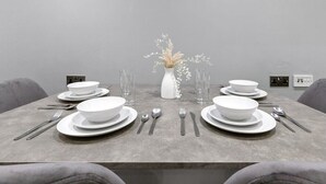 Une table à manger dressée avec de l’assiette, des bols et des couverts blancs, agrémentée d’un vase blanc et de fleurs séchées placés au centre.