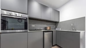 Una cocina moderna con armarios grises, horno empotrado, lavavajillas y pileta.