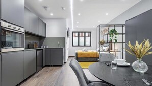 Una cocina moderna con armarios grises, horno empotrado y comedor con una mesa y sillas oscuras.