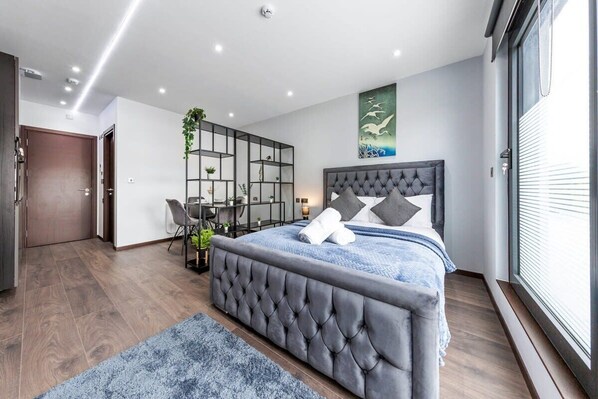 A modern bedroom with a large bed, a desk, and a shelving unit.