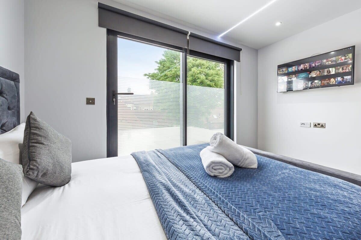 Et moderne hotelværelse med en stor seng, udsigt gennem en skydedør og et vægmonteret tv, der viser forskellige kanaler.