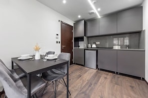 A modern kitchen with grey cabinets, a built-in oven, and a dishwasher. There is a dining table with chairs and a vase with dried flowers.