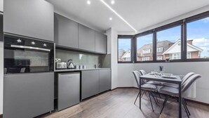 A modern kitchen with grey cabinetry, a built-in oven, and a dining area with a table and chairs.