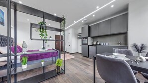 A modern living room with a sofa, a dining table, and a kitchen area with cabinets and appliances.