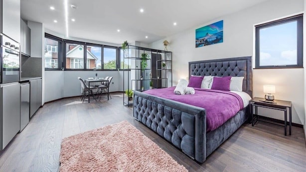 A modern bedroom with a large bed, a dining area, and a kitchen.