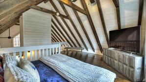 A bedroom with a sloped ceiling, a bed with a patterned bedspread, a television on a wooden stand, and a bench. - Picture Perfect | Hot Tub + Fireplace + Mtn Views (Blue Ridge)