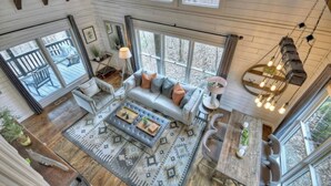A spacious living room with a large sofa, a coffee table, and a dining area with a wooden table and chairs. - Picture Perfect | Hot Tub + Fireplace + Mtn Views (Blue Ridge)