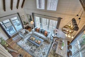 A spacious living room with a large sofa, a coffee table, and a dining area with a wooden table and chairs. - Picture Perfect | Hot Tub + Fireplace + Mtn Views (Blue Ridge)