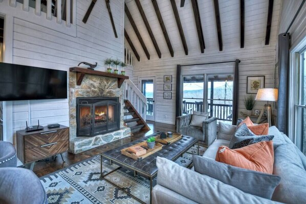 A cozy living room with a stone fireplace, a flat-screen TV, and a comfortable seating area with a sofa and cushions.