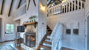 A spacious living area with a stone fireplace, wooden staircase, and a white railing. - Picture Perfect | $179 Off Your Stay! (Blue Ridge)