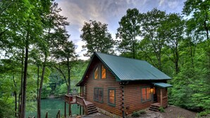 Eine Blockhütte mit Metalldach, einer Holzterrasse und einem Teich im Hintergrund.