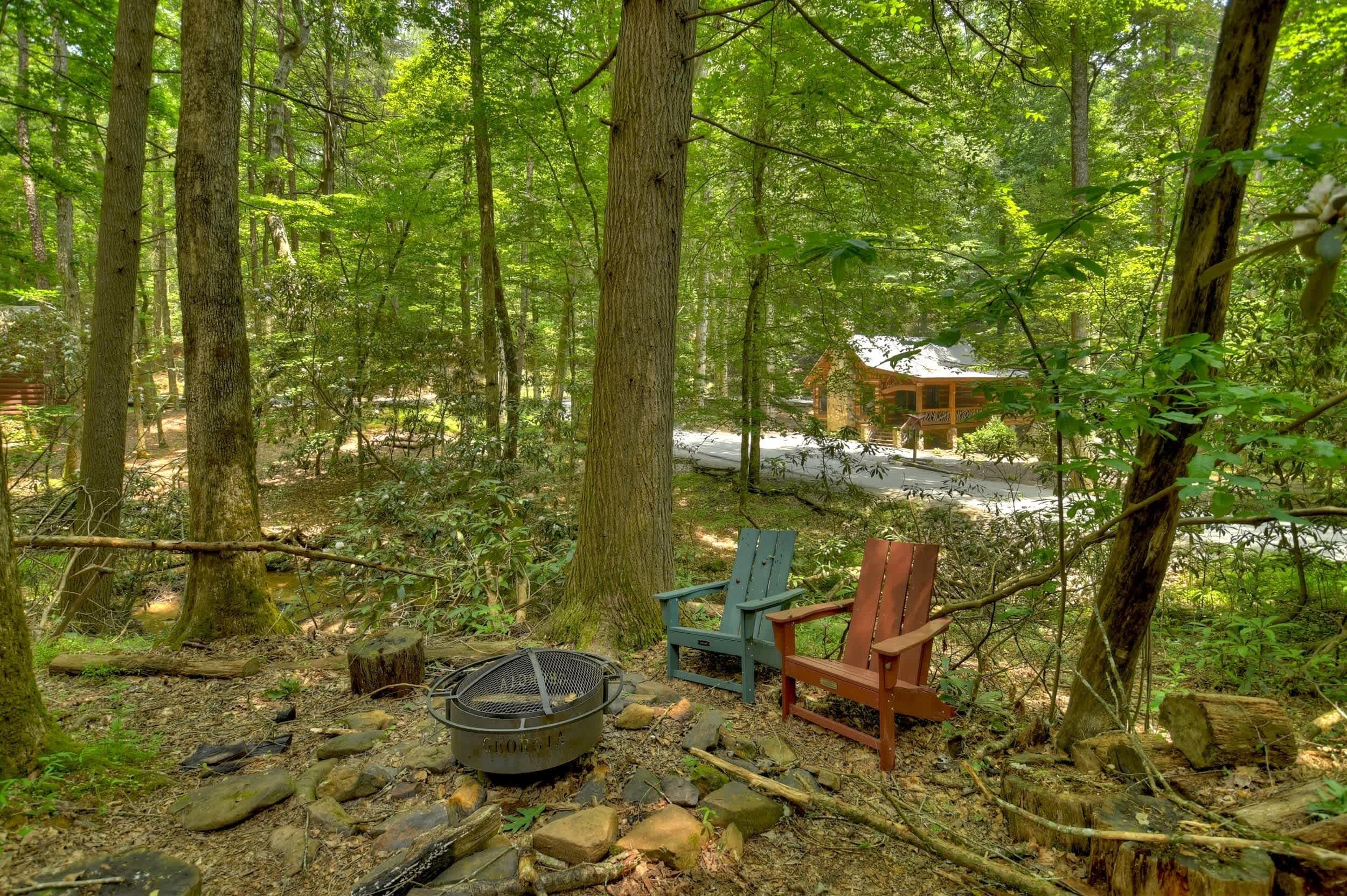 A forest cabin with a fire pit and two Adirondack chairs.