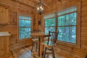 Cozy cabin with a round dining table and four chairs, surrounded by large windows offering a forest view.