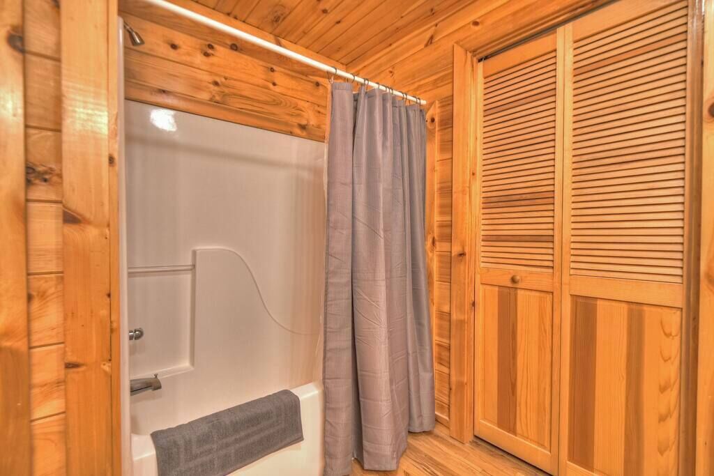 Een houten badkamer met een bad, een douchegordijn en een houten deur.