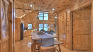 Ein großzügiges Blockhaus-Interieur mit einer zentralen Essecke, Holzwänden und großen Fenstern.