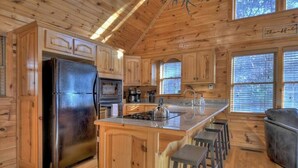 Ein Holzblockhaus-Innenraum mit einer Küche, die einen Kühlschrank, einen Backofen und Barhocker beinhaltet.