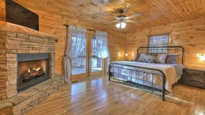 Ein gemütliches Schlafzimmer in einer Blockhütte mit Kamin aus Stein, einem Bett mit Metallgestell und einem Deckenventilator.