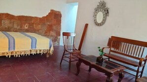 Une pièce comprenant un lit, une chaise en bois, un banc en bois et un miroir accroché au mur.
