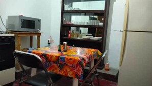 Une petite cuisine équipée d’un four à micro-ondes, d’une table recouverte d’une nappe colorée, d’une chaise et d’un réfrigérateur.