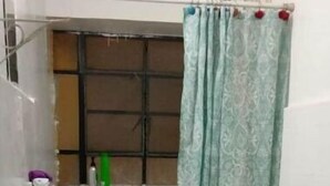 Une petite salle de bain avec un lavabo blanc, des toilettes et une fenêtre ornée d’un rideau à motifs.