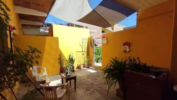 Un espace patio avec des murs jaunes, une table en bois, des chaises, des plantes en pot et un auvent blanc qui offre de l’ombre.