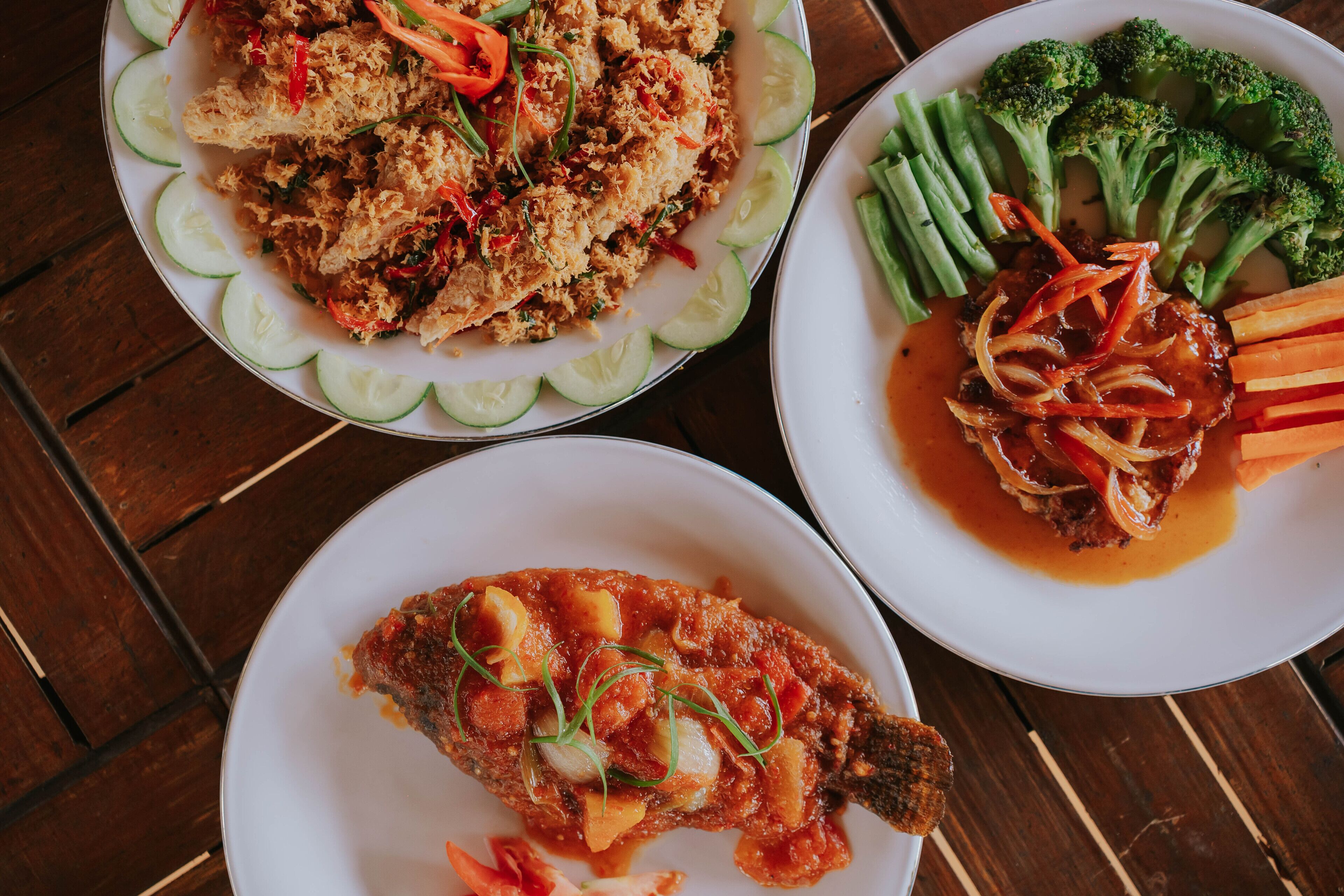 Tres platos de comida con diferentes verduras y un pescado.