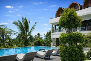 A pool area with lounge chairs, surrounded by lush greenery and a modern building with arched windows. - Nirvana Hotel Resort Tetebatu (Tetebatu)
