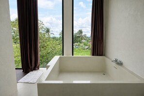 A modern bathroom with a large bathtub, a window with curtains, and a view of greenery outside. - Nirvana Hotel Resort Tetebatu (Tetebatu)