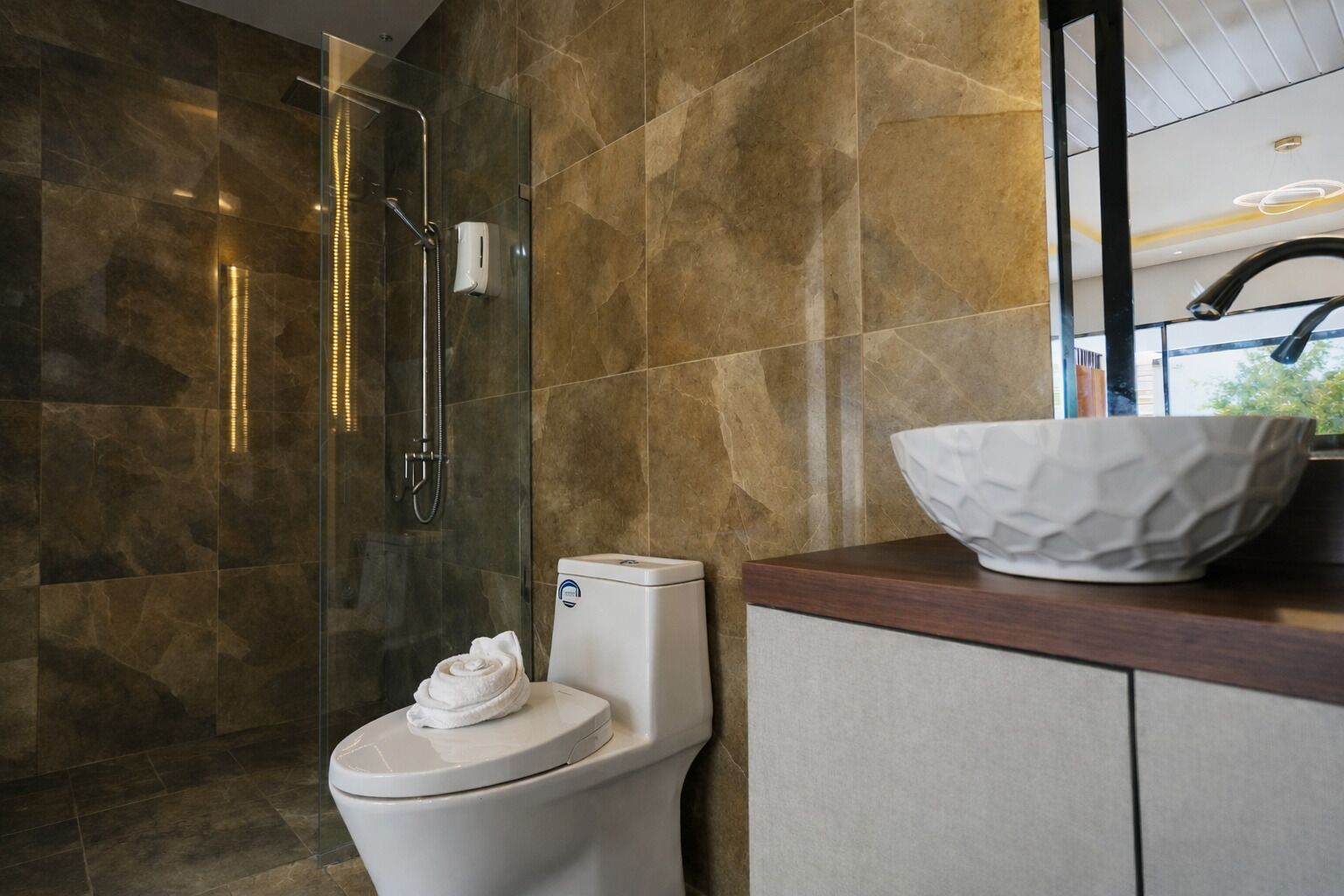 Un baño moderno con ducha de vidrio, inodoro blanco y tocador de madera con lavabo blanco.