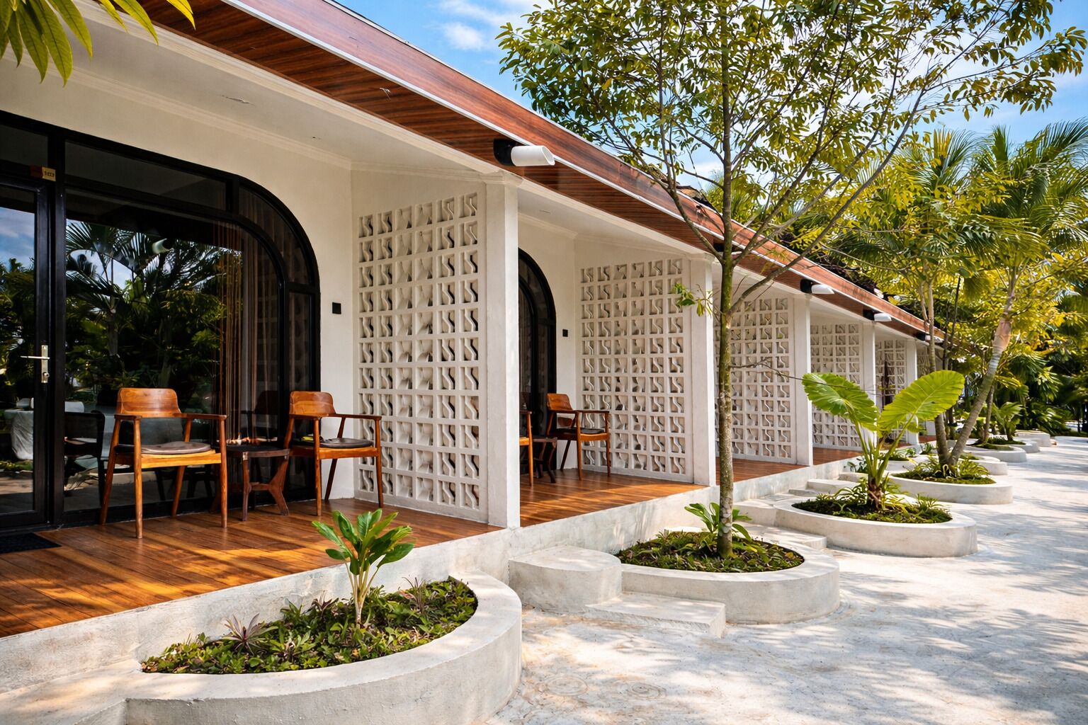 A covered outdoor seating area with wooden chairs and planters, a white wall with a geometric pattern, and a wooden ceiling.