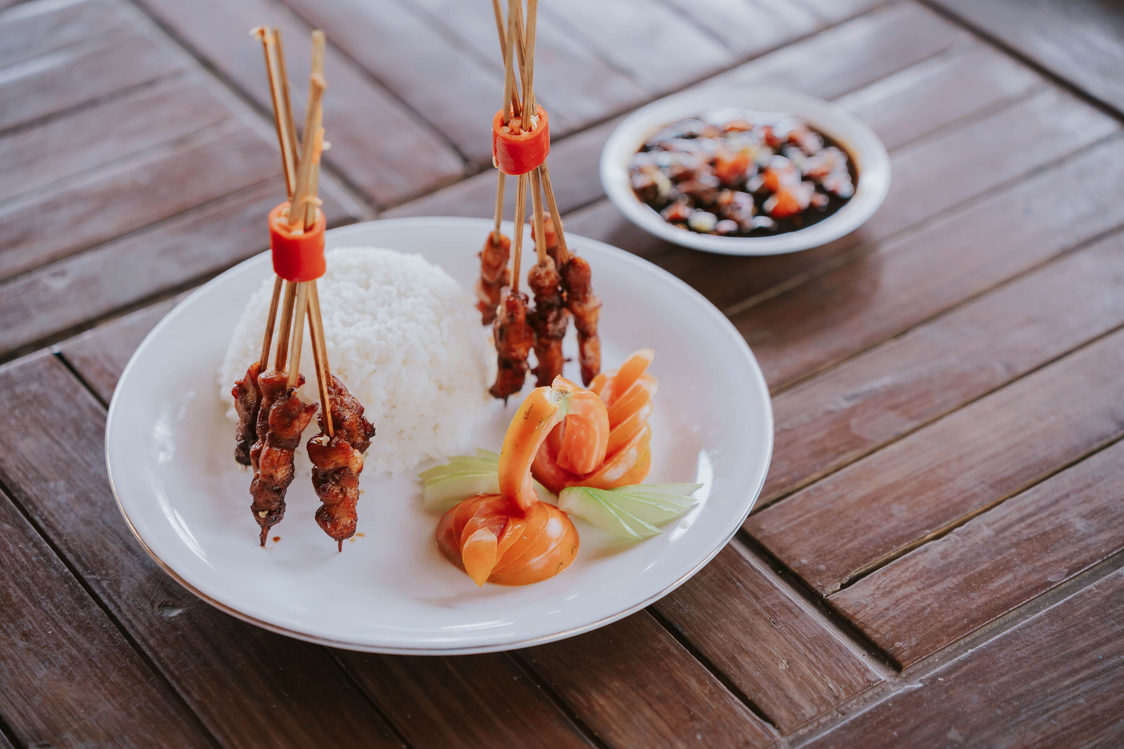 A plate with skewers of meat, rice, and vegetables on a wooden table.