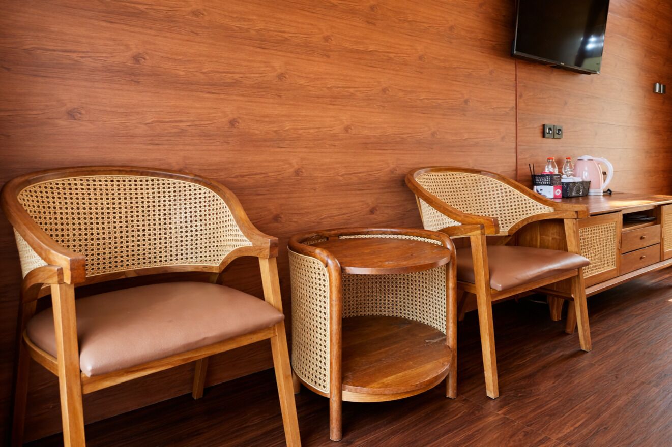 A room with two wicker chairs, a small round table, and a wooden cabinet with a flat-screen TV mounted on the wall.