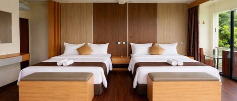 A modern hotel room with two beds, wooden flooring, and large windows offering a view of greenery.