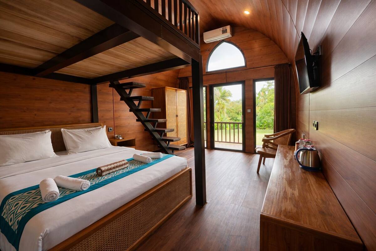 Una habitación estilo cabaña de madera con cama, escalera, zona de comedor y vistas al exterior.