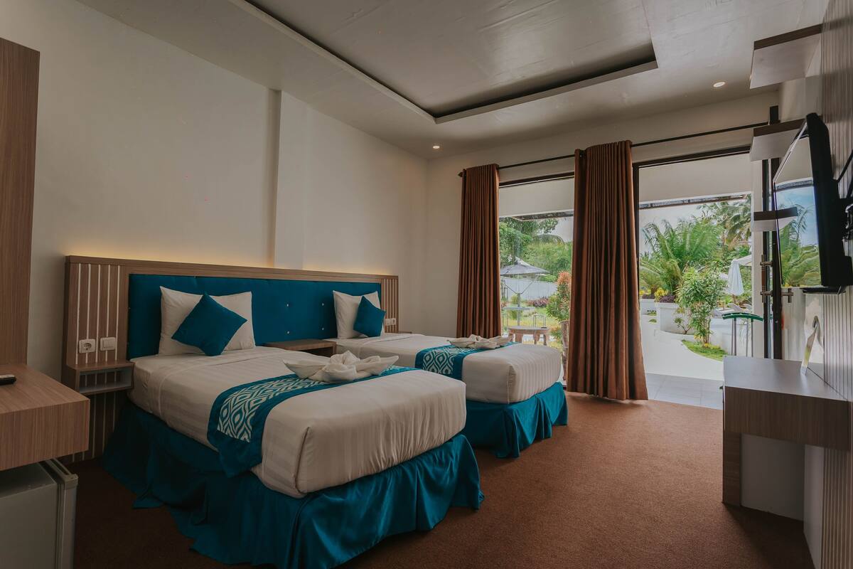 Habitación de hotel con dos camas, un escritorio y vistas al exterior.
