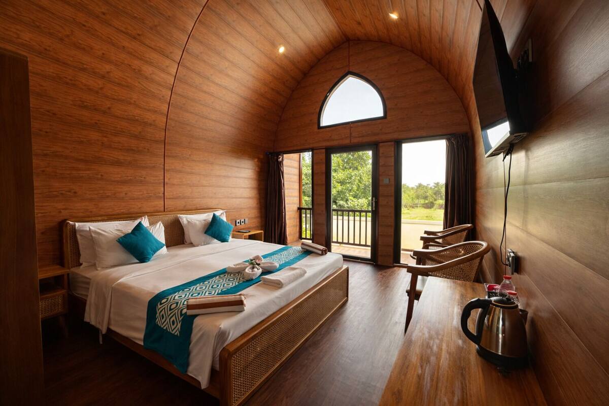 Un dormitorio amplio con una cama grande, techo de madera y vistas al exterior desde una puerta abierta.
