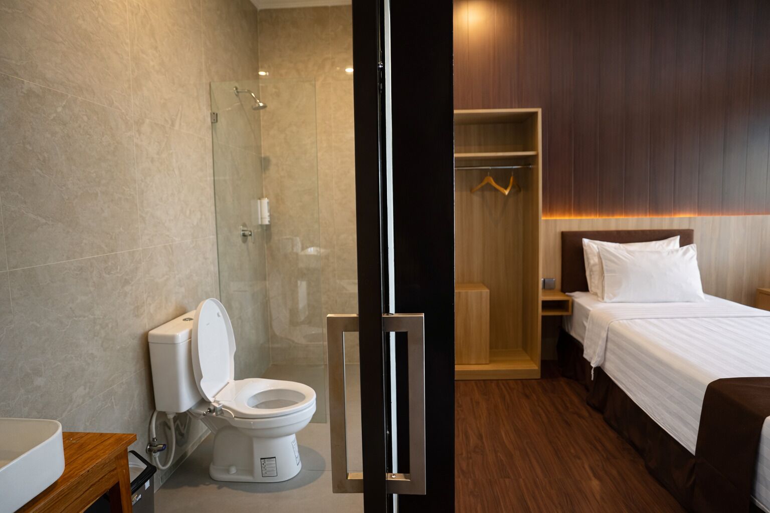 A modern hotel room with a shower, toilet, and a bed with a wooden headboard.