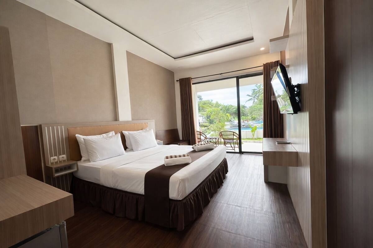 Habitación de hotel con una cama grande, un escritorio, un televisor montado en la pared y vistas al exterior.