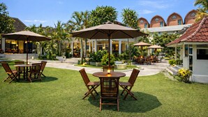 A well-maintained outdoor patio area with tables and chairs, surrounded by lush greenery and palm trees. - Nirvana Hotel Resort Tetebatu (Tetebatu)
