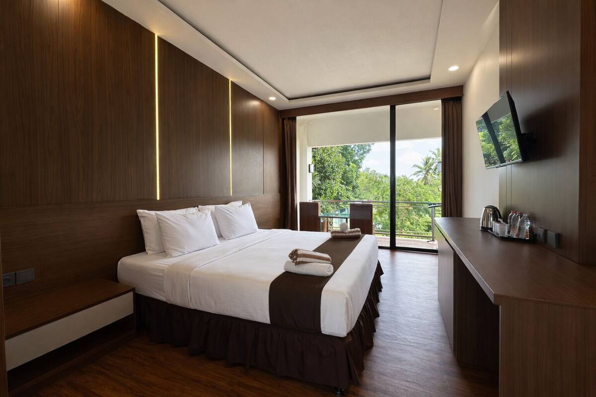 Habitación de hotel moderna con una cama grande, un escritorio y un balcón con vistas a zonas verdes.