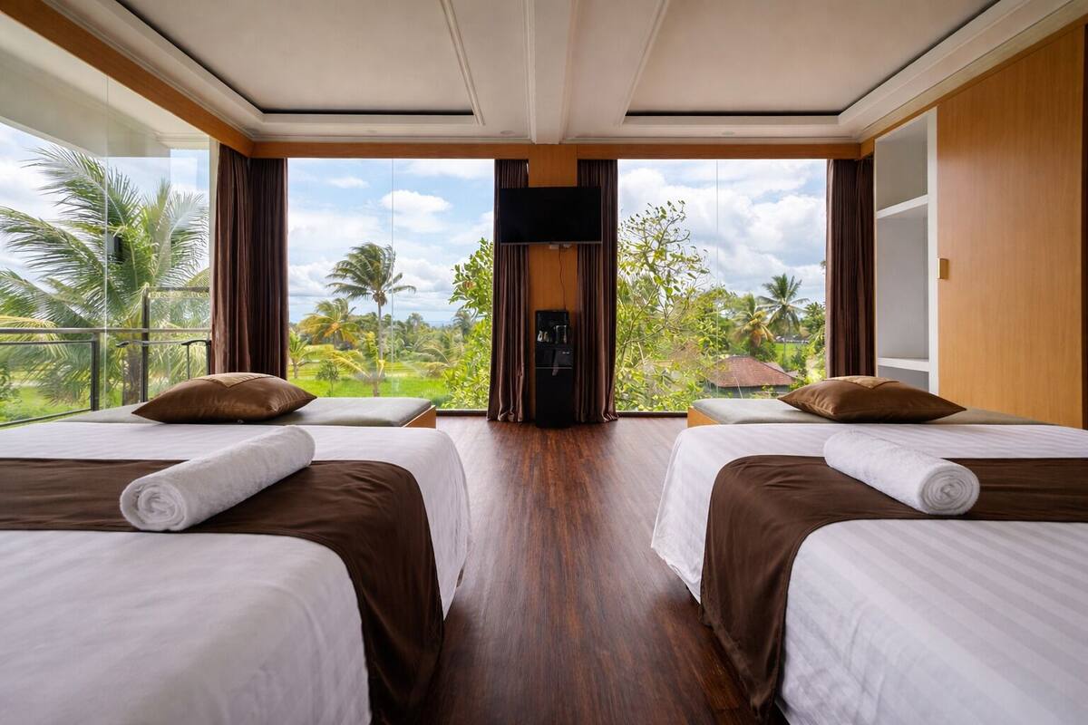 Una habitación de hotel con dos camas, televisión y vistas a palmeras.