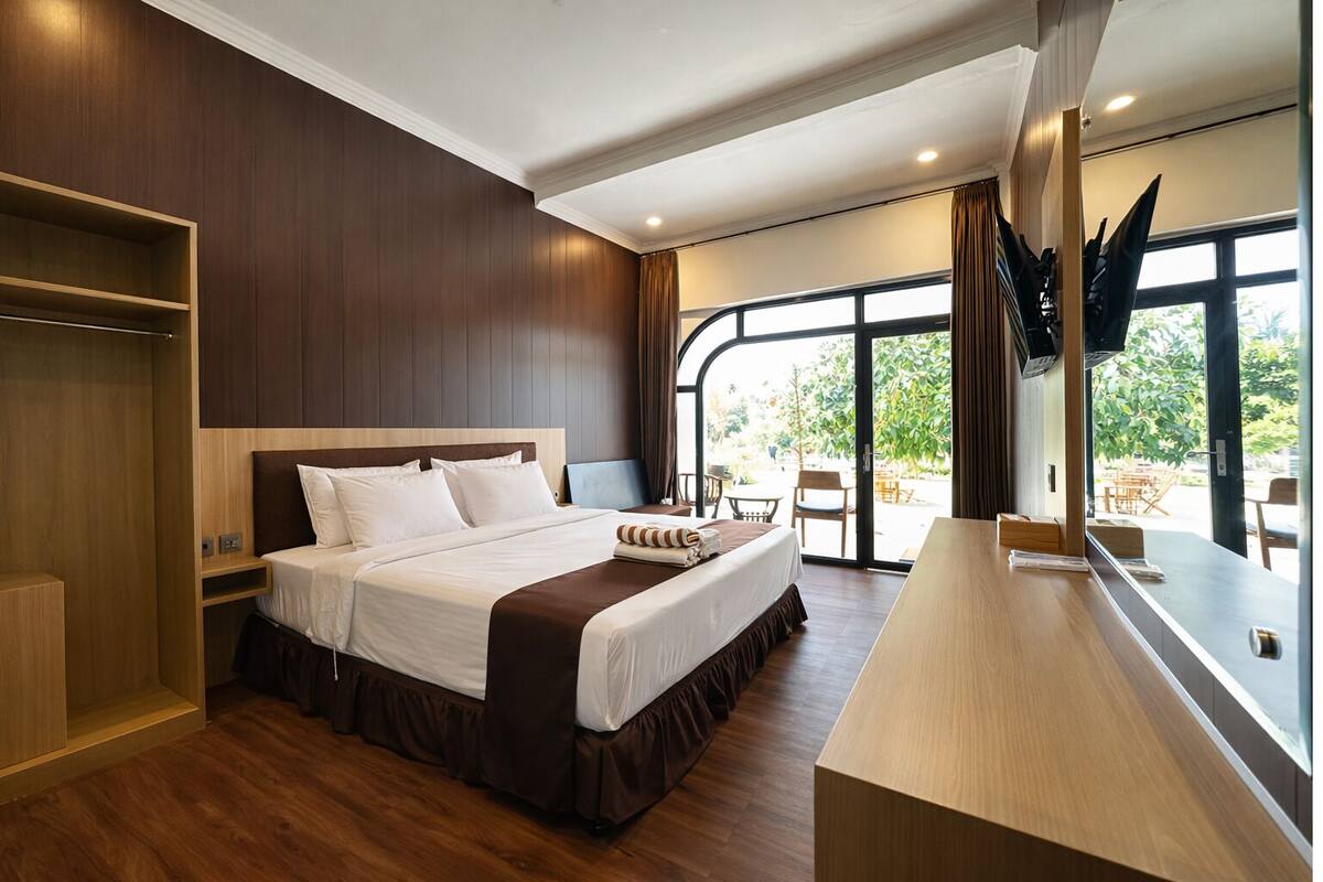 Habitación de hotel moderna con una cama grande, piso de madera, armario empotrado y balcón con mobiliario exterior.