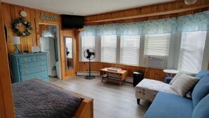 Quarto aconchegante com paredes de madeira, uma cama, um sofá azul, um aparador e um ventilador.