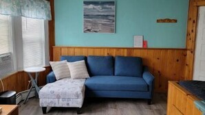 Um quarto aconchegante com um sofá azul, uma mesa pequena e uma janela com persianas.