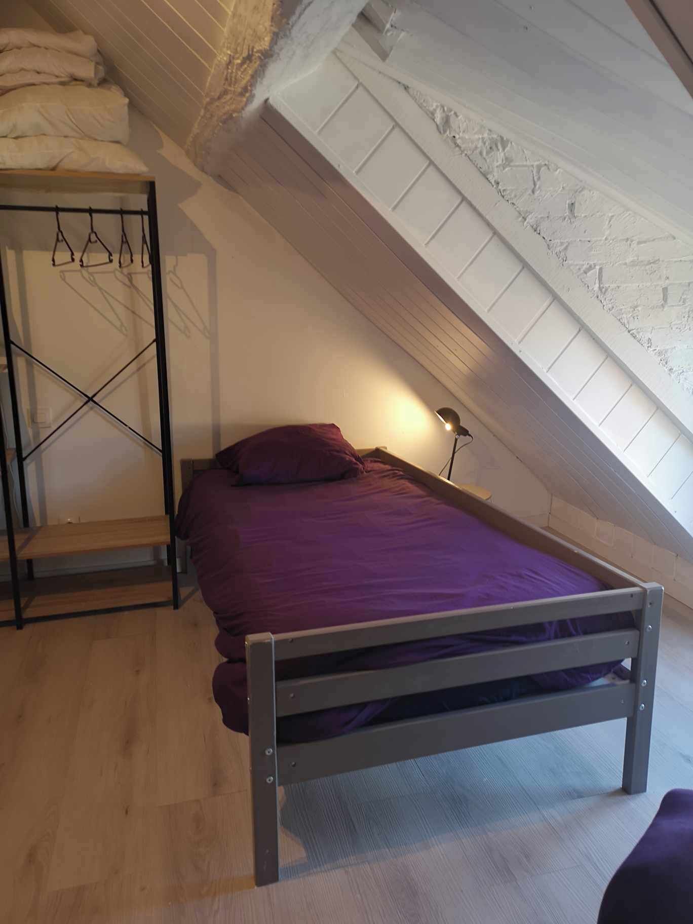 A small, single-bed room with a sloped ceiling, wooden flooring, and a bed with a purple bedspread.