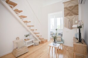 Uma sala de estar moderna com escada de madeira, uma mesa pequena com um vaso e uma cadeira.